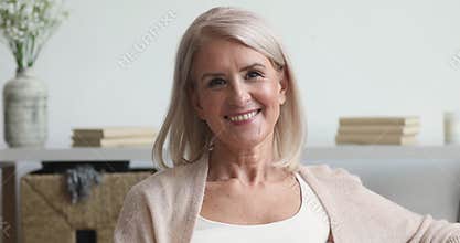 Happy older middle aged woman looking at camera at home