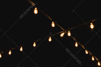 Light bulb decor in outdoor party. Decorative outdoor string lights at night time. Golden glowing garlandon in wedding