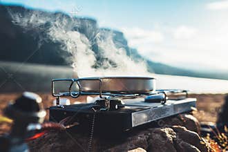 Camping cooking in nature outdoor, prepare breakfast picnic in mist morning; cooker food metal gas stove on stone; tourism