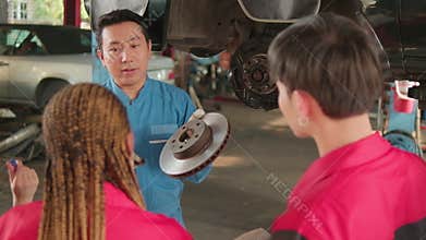 Supervisor engineer is teaching mechanic workers about car repair at a garage.