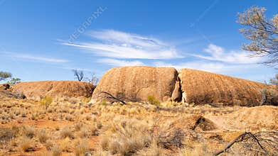 Large smooth granite outcrop between dry grass and blue sky