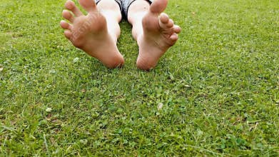 Child boy is lying on a green grass in the park on a sunny day in nature with barefoot dirty legs