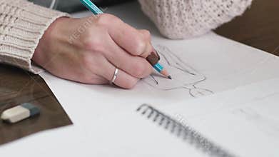 Fashion designer drawing model for clothes sketch. Hand of female tailor drawing pattern at paper in her studio.