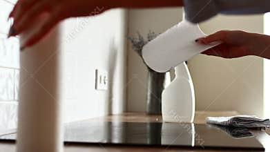 Delicate cleaning induction electric stove. Housewife cleans kitchen hob with cleaning spray with mockup and paper