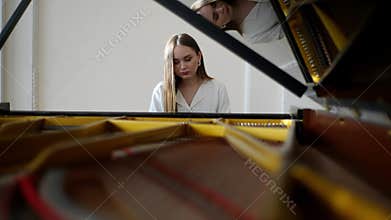 Selective focus view from open lid of music instrument to attractive young female pianist wearing elegant casual clothes