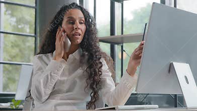 Young multitasking businesswoman speaks on mobile phone communicates with client looks at monitor screen woman manager
