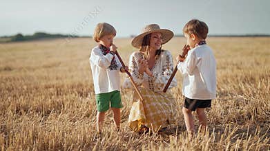 Boys playing on wooden flutes - sopilka. Ukrainian mother with children sons in wheat field. Woman in embroidery
