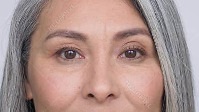 Mature asian woman looking at camera advertising under eye skin care.