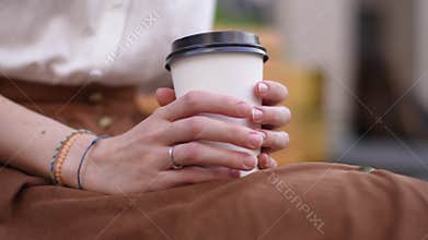 Close-up cropped shot of unrecognizable young woman tapping nervously holding in hands takeaway cup of hot coffee while