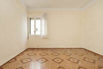 Empty living room with cream painted walls, brown vintage tile floors with borders and window with white sheers