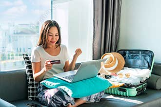 Happy Asian woman using credit card booking flight tickets and hotel at home. Planning a trip and online booking concept