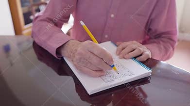 Man With Arthritis Using Grip Aid On Pencil To Write In Sudoku Puzzle Book
