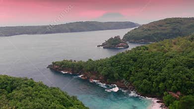 Beautiful aerial copter footage of ocean lagoon with pink sand beach and wild woods under pink sunrise sky in the