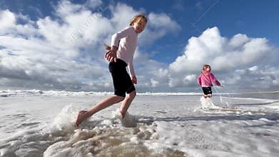 Children run along the coast of the Atlantic Ocean. Two little sisters are playing with the waves on the beach of the