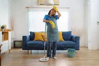 Exhausted Asian maid struggles with fatigue while mopping the house, showcasing the challenges and hard work behind domestic house