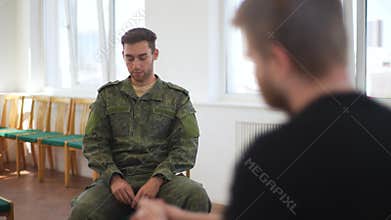 Tracking shot of depressed young bearded soldier male in camouflage uniform sitting on chair telling story to PTSD