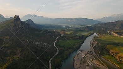 aerial scenic landscape with green fields, meadows, curved mountain river and mountain ridge with high mountains and