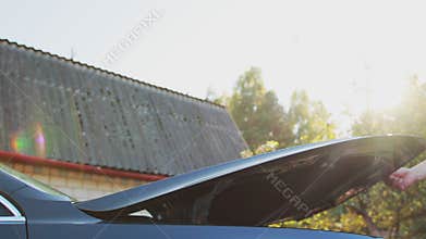 A male driver closes the hood of a car against the backdrop of the sun. Checking technical fluids in the engine