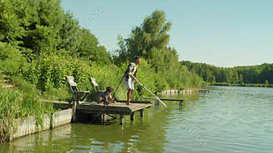 Excited teenage fisherman and dad with fishing rod catching fish on lake