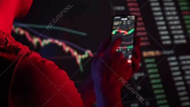 Trader Analyzes Cryptocurrency Charts on a Smartphone Screen in the Dark