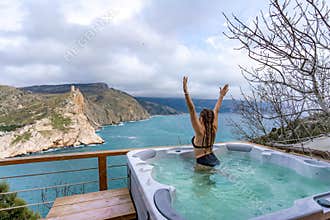 Outdoor jacuzzi with mountain and sea views. A woman in a black swimsuit is relaxing in the hotel pool, admiring the