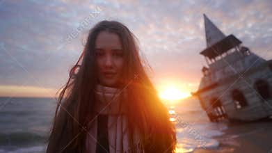Happy smiling mixed ethnic woman looking at camera standing on beach with old flooded wooden house, chapel washed by sea