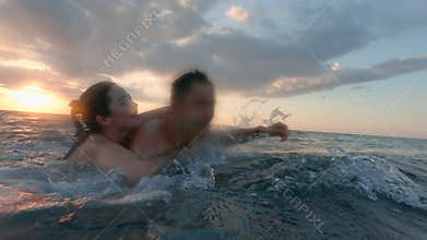 A happy couple bathing at sunset in green ocean. Pretty girl riding her boyfriend's back as he is swimming in warm
