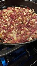 Corned beef hash being fried in cast iron skillet on a gas stove.