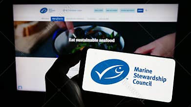 Person holding cellphone with logo of organization Marine Stewardship Council (MSC) on screen in front of webpage.