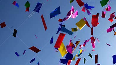 Vibrant pieces of confetti gently float down from a clear blue sky, creating a celebratory atmosphere and marking a special moment