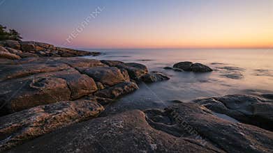 Serene Coastal Scene Featuring Rocks Sea and a Sunset Sky in Warm Colors