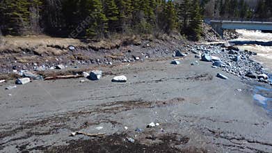 A camping trailer is set up near a road at the mouth of a river and a bridge near a sandy beach at low tide.