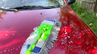 Car detailer cleaning red car hood with special mop