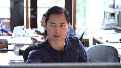 Architect Working At Desk With Meeting In Background
