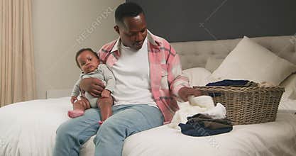 Loving Father Holds Baby While Folding Laundry on Bed: A Heartwarming Scene of Parenthood