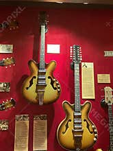 Collection of vintage guitars displayed on red background, arranged in two rows, each with informational placards Bright and even