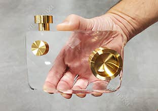 Handheld view of a modern, clear acrylic see-through camera model with gold details