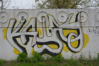 A bright,The graffiti depicting the word in Russian KASHAU, ????? is painted on a white and gray concrete fence.