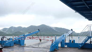 Ferry Ramp with Blue Structure Facing Misty Mountain Shore on Overcast Day
