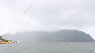 Panning Misty Island View Over Calm Sea with Docked Boats and Overcast Sky