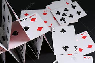 Collapsed house of playing cards on black background, closeup