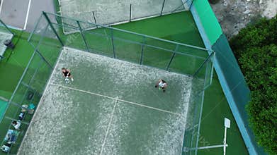 Aerial view of people playing padel tennis on a professional court. The drone captures the dynamic movement of the