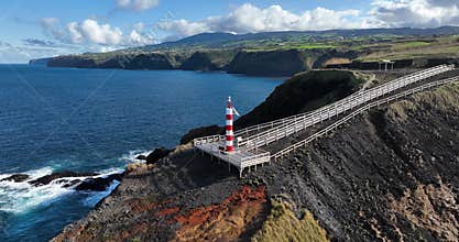 Small lighthouse on rugged cliff line of the Azores, Sao Miguel, shipping beacon, vulcanic rocks, aerial drone video