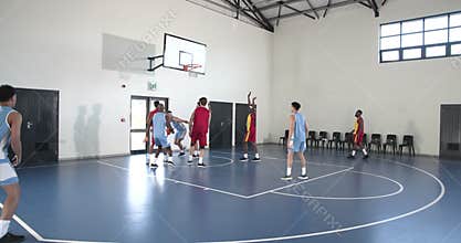 Basketball players competing intensely on indoor court, aiming for hoop