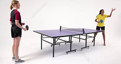 Playing table tennis, two women competing intensely in studio setting