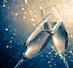 Two champagne flutes with golden bubbles on blue light bokeh background