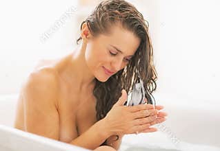Happy young woman applying hair conditioner in bathtub