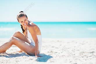 Smiling young woman sitting on beach and looking on copy space