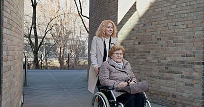 Young caregiver pushing elderly woman in wheelchair outdoors