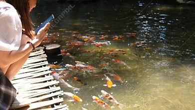 Woman Using Smartphone by Koi Pond in Serene Garden